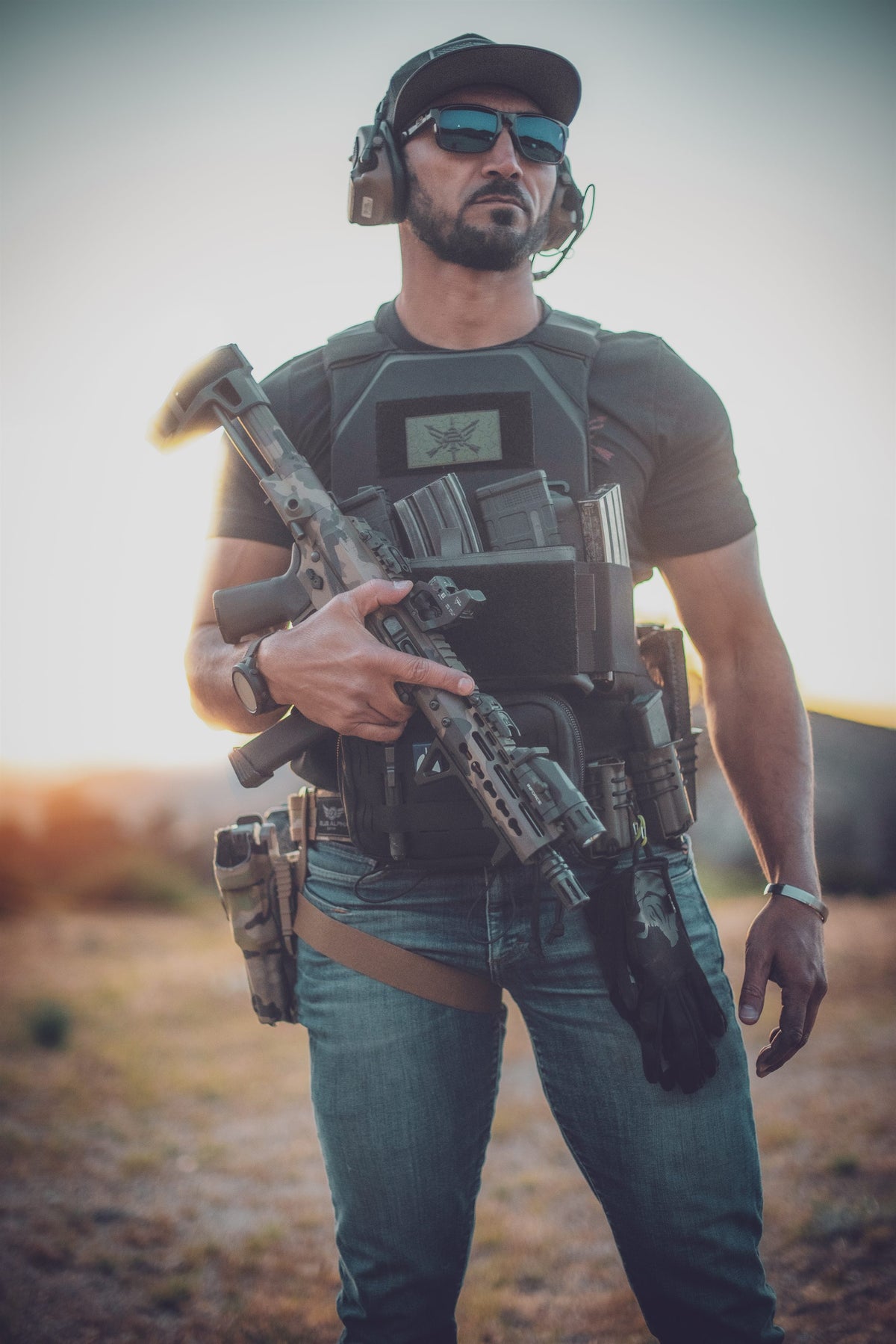 A shooter wearing a plate carrier, battle belt and holster, holding a rifle.