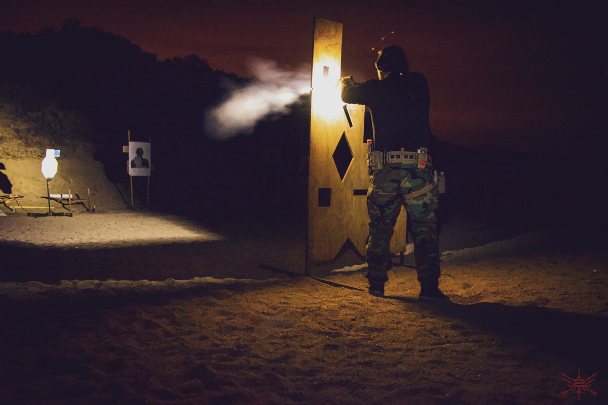A shooter firing from behind a barricade at night, muzzle flash visible.