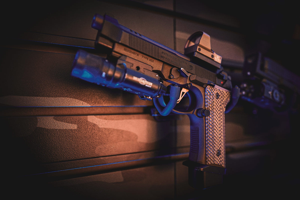 A pistol fitted with a red dot optic and weapon light, photographed in low blue light.